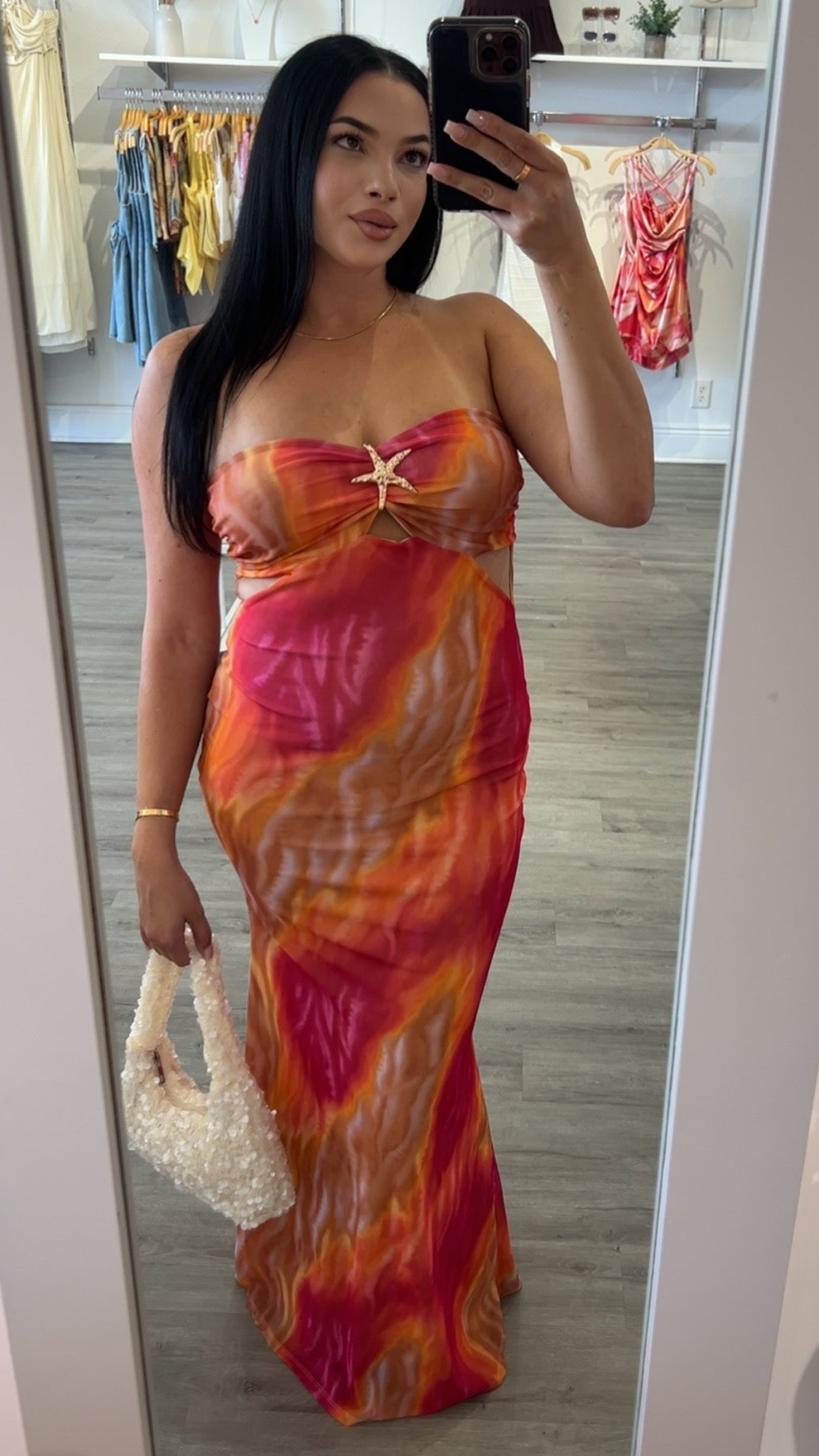 Woman wearing the Starfish Maxi Dress featuring a vibrant orange and pink tropical sunset print with a strapless neckline and gold starfish detail, perfect for summer vacations and resort wear.