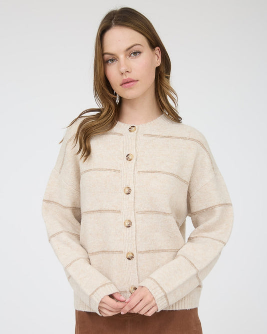 A woman modeling a cream-colored knit cardigan with horizontal textured stripes and gold buttons, paired with a brown mini skirt, against a light gray studio background.