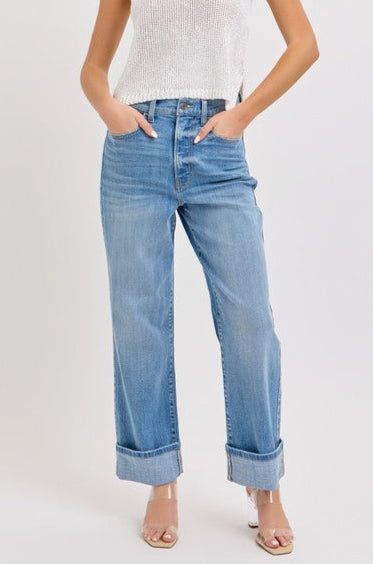 Woman wearing a white sleeveless top and medium blue jeans on a plain background