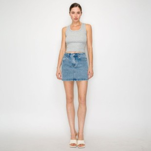 A model stands against a light gray studio background wearing a light gray ribbed tank top, a light-wash blue denim mini skirt, and white heeled sandals.